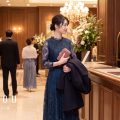 冬の結婚式会場のクロークでコートを預ける、ネイビーのレースドレスの女性