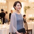 披露宴会場に立つ、ショートヘアにブルーグレーのレースドレスとショールを合わせた親族の女性